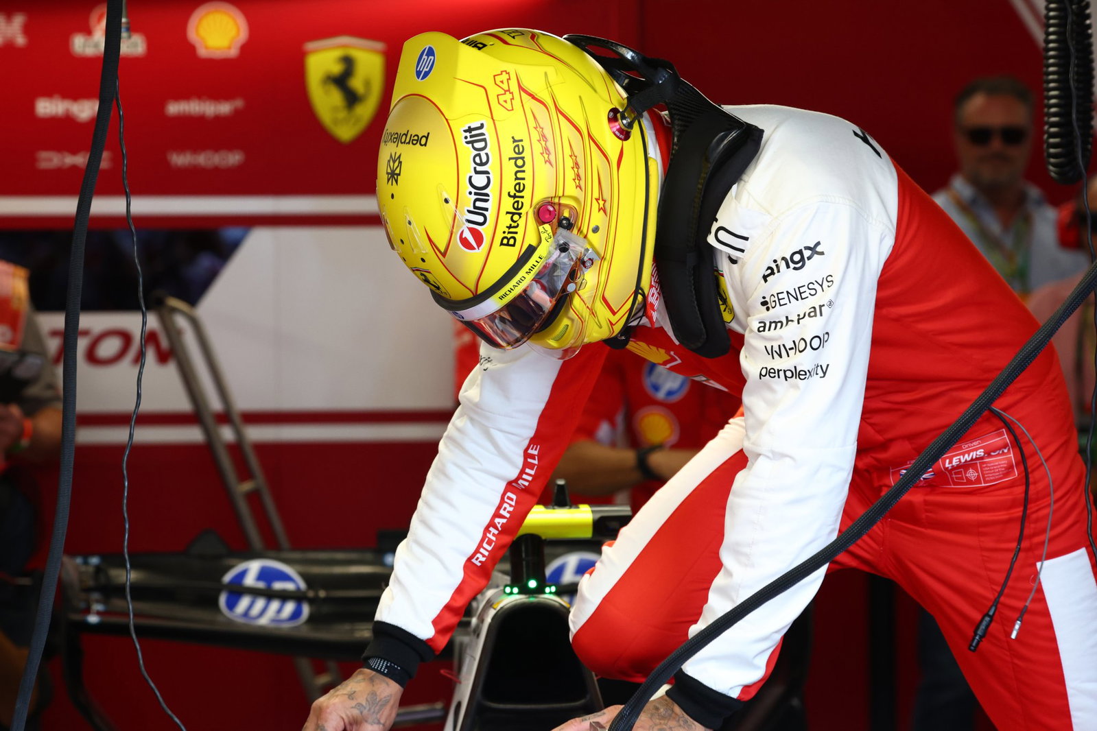 Lewis Hamilton đội mũ bảo hiểm vàng cúi người bên chiếc Ferrari trong garage