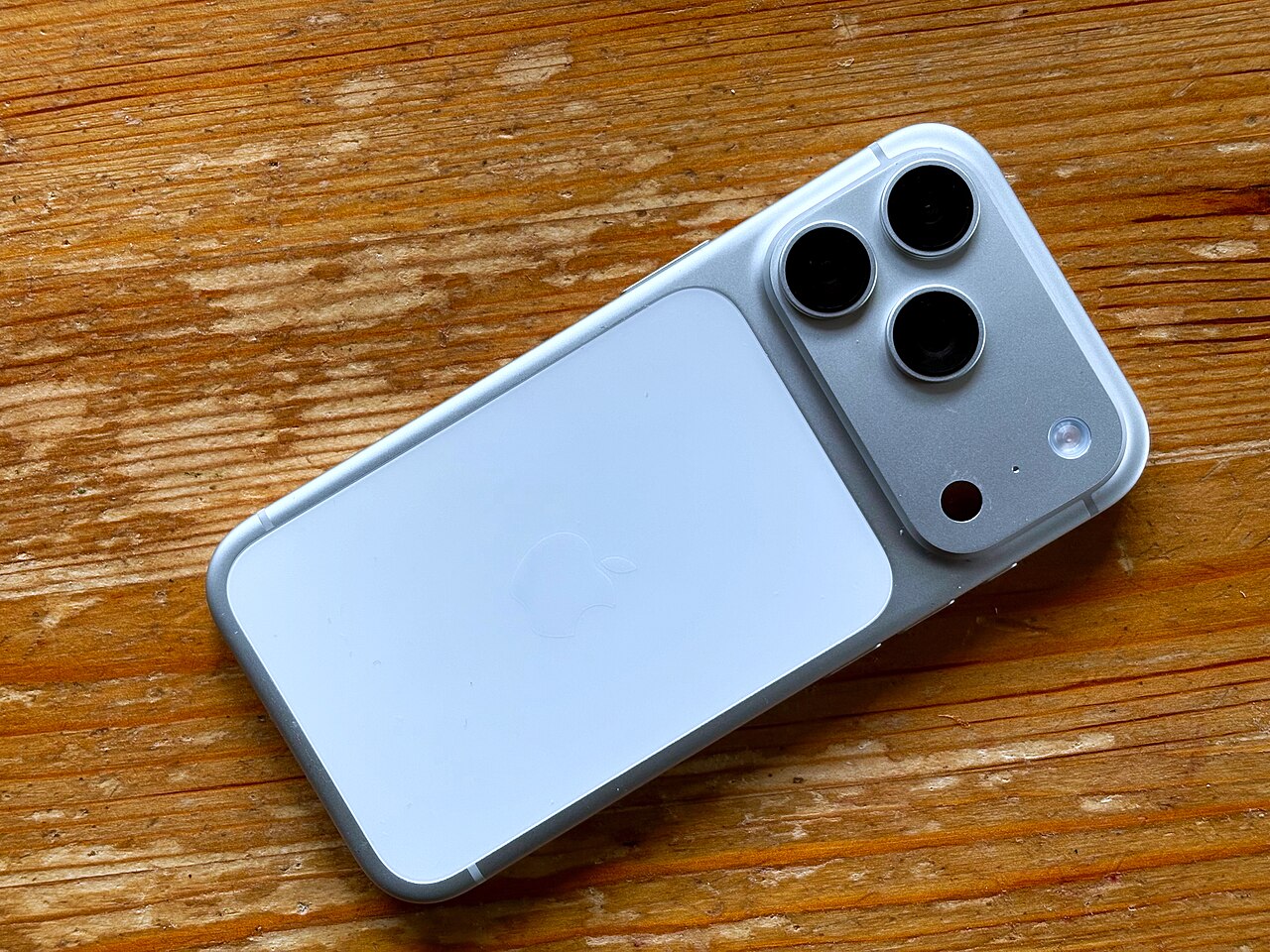 iPhone 17 Pro màu bạc đặt úp trên bàn gỗ, cụm ba camera và mặt lưng kính
