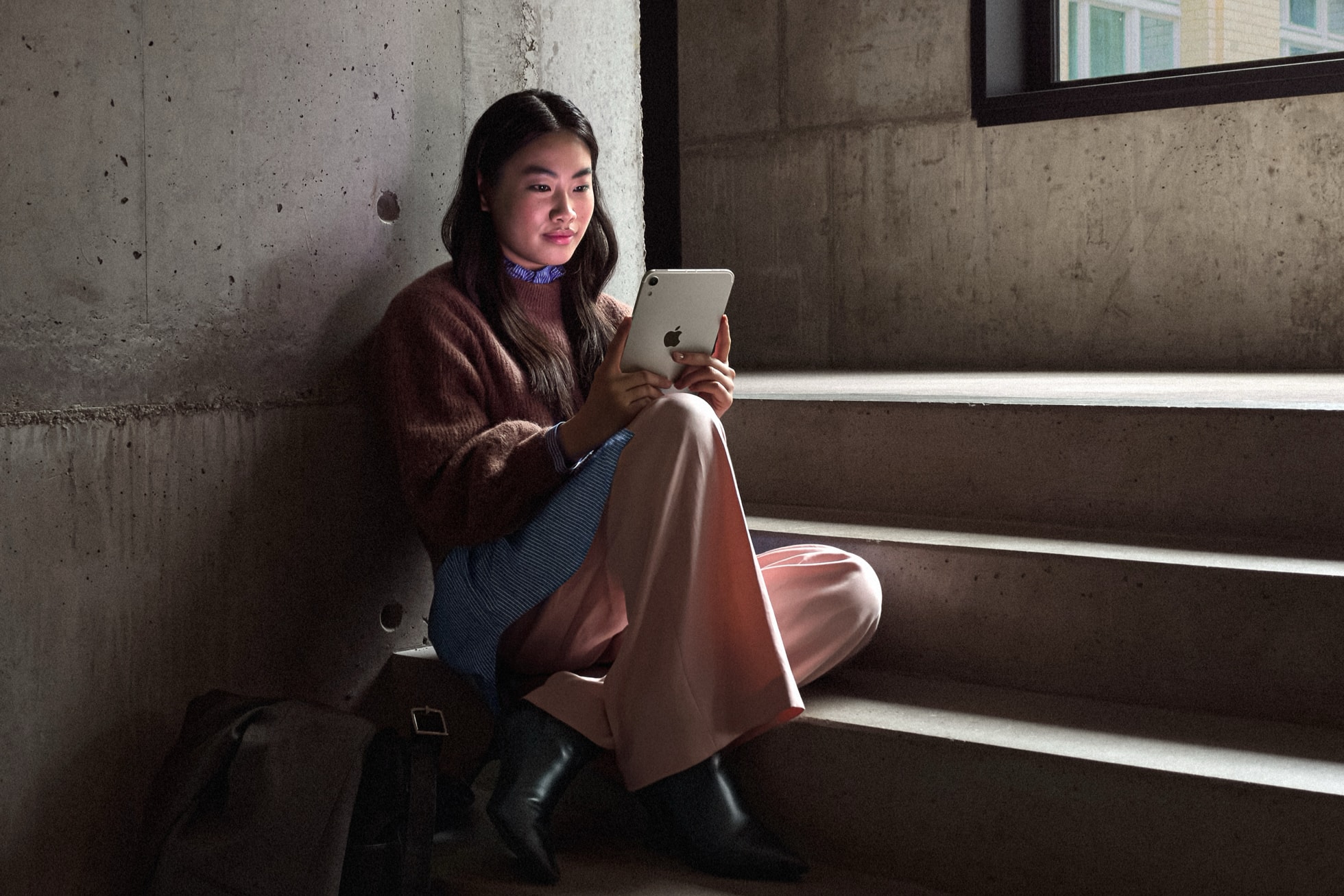 Người dùng ngồi đọc trên iPad mini OLED màu Ánh Sao, mặt lưng có logo Apple và camera đơn