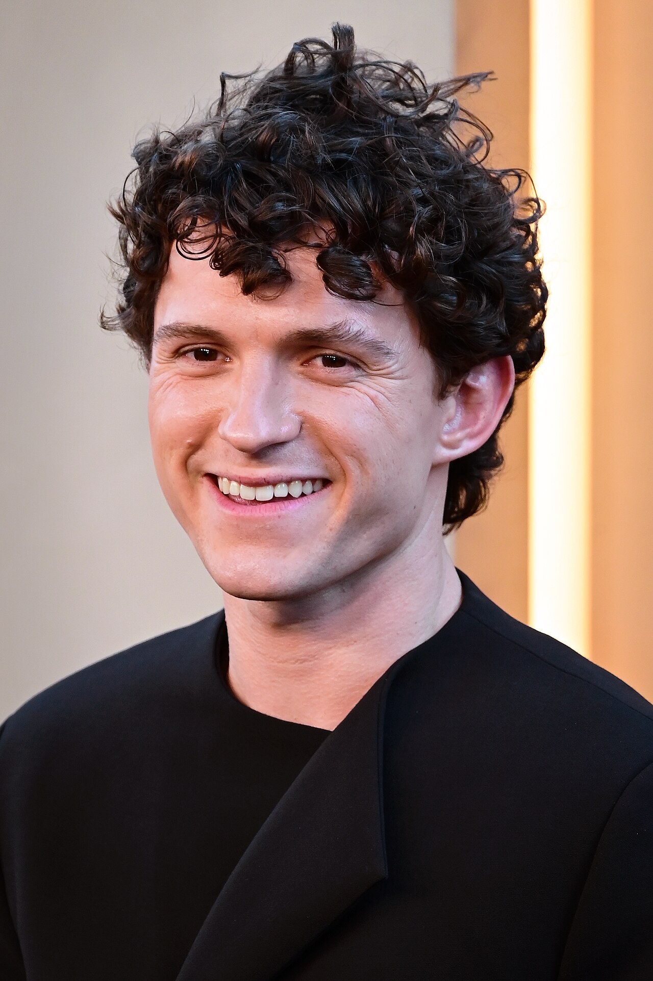 Tom Holland mặc áo đen cười trước phông nền tại buổi ra mắt The Odyssey ở New York